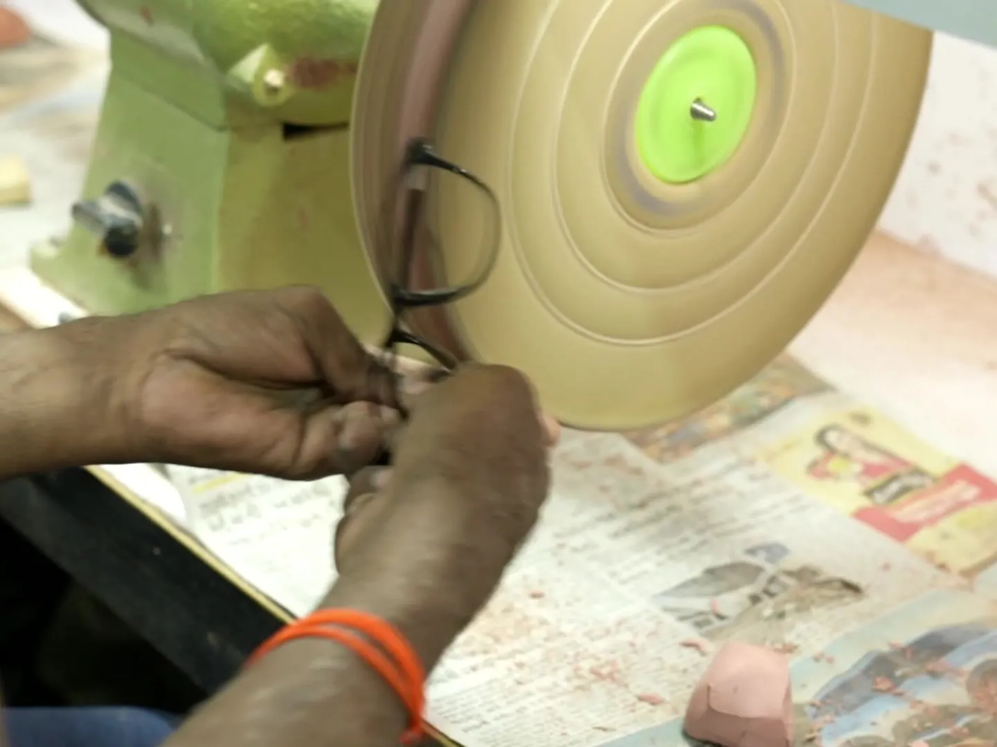 Worker finishing the edge of an acetate frame front against a polishing wheel at the RTC Eyewear workshop in Ahmedabad